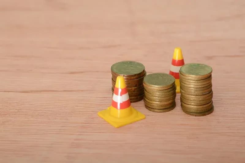 Stacks of gold coins flanked by miniature traffic cones on a wooden surface, symbolizing construction costs and budgeting