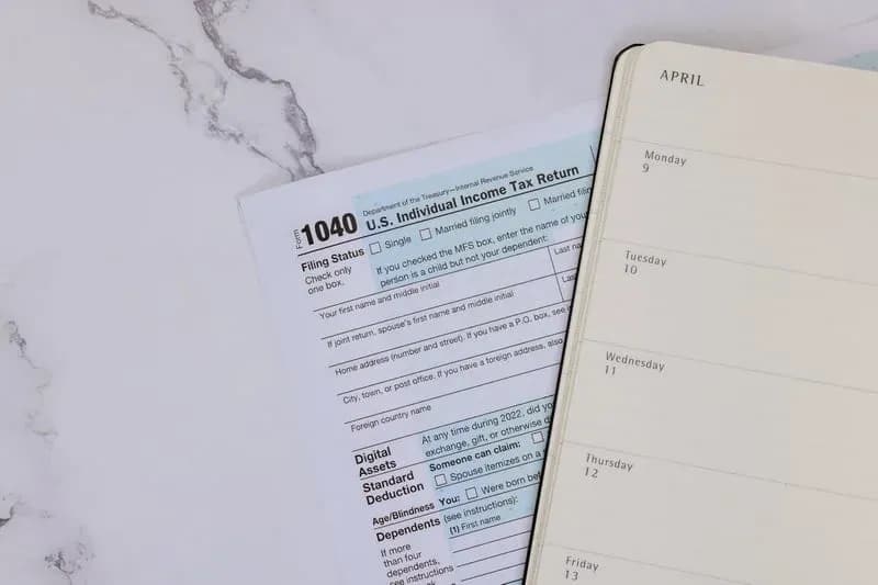 Form 1040 tax return beside an open April weekly planner on a marble desk