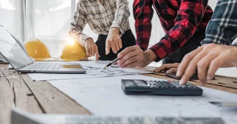 Contractors reviewing blueprints and job costs with a calculator and laptop — Construction Bookkeeping from RDP Bookkeeping Solutions